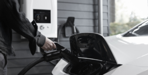 A man charging an EV at his home charging station. Black and gray image.