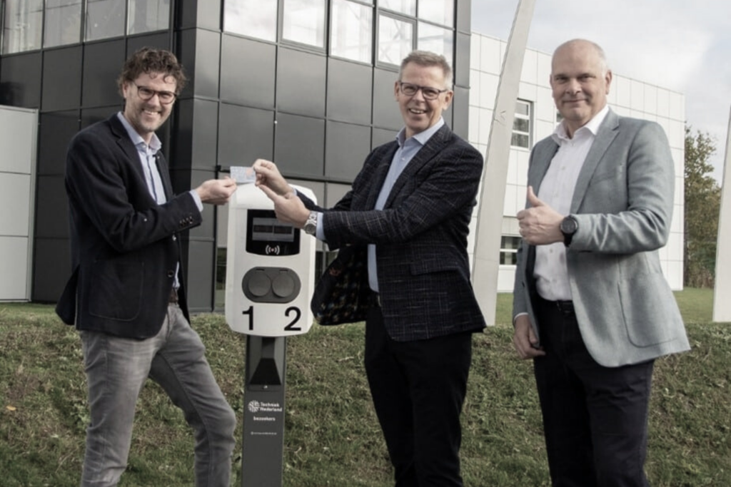 Three men standing near a Connectned electric car charger, with one holding a charge card.